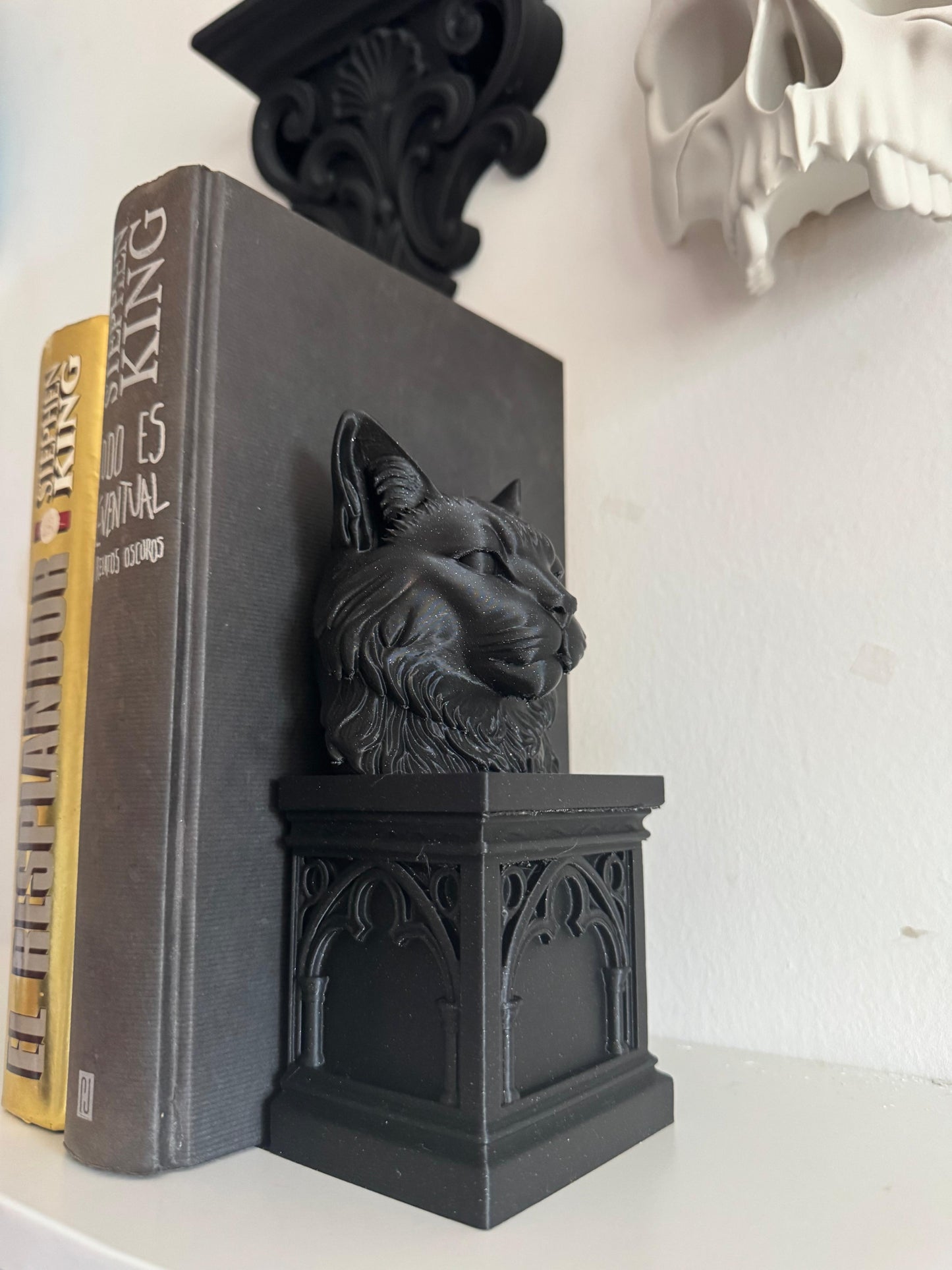 Black cat-shaped bookend on a book with a skull decoration in the background