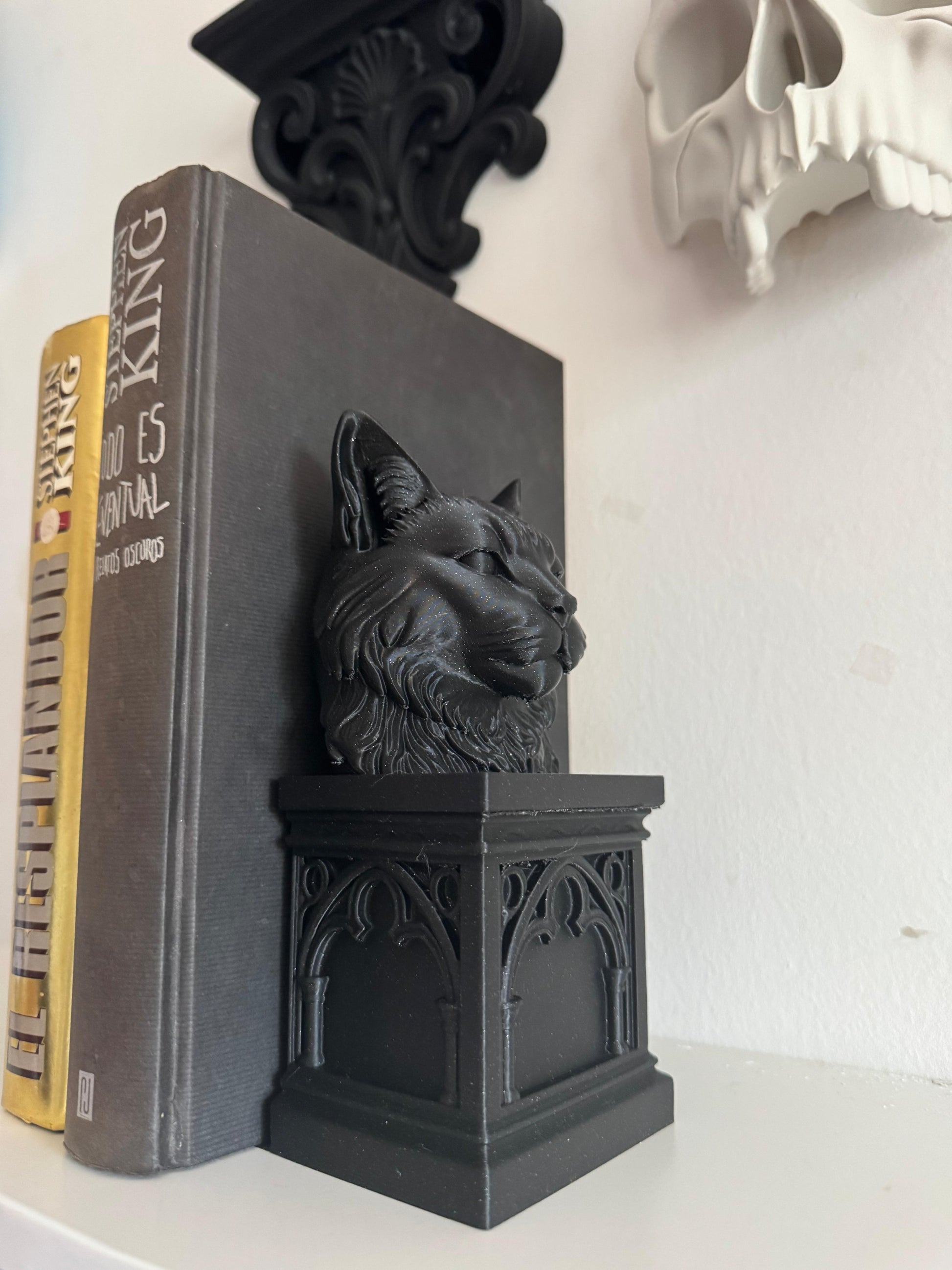Black cat-shaped bookend on a book with a skull decoration in the background