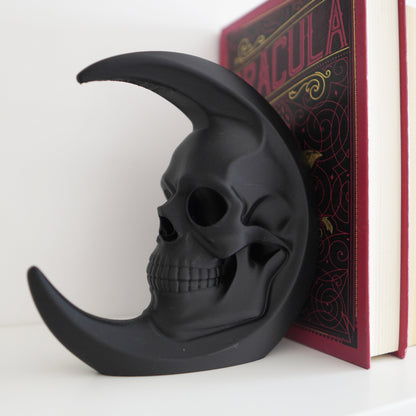Black skull-shaped object on a white surface with a book titled 'Dracula' in the background.